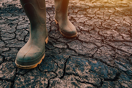 Farmer in rubber boots walking on dry soil ground