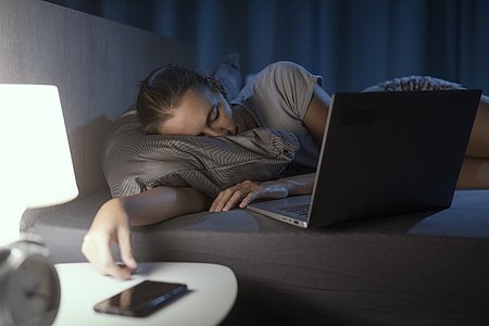 Woman falling asleep in front of her laptop in bed